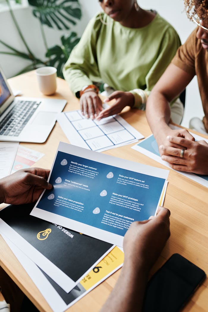 Team members collaborate over documents in an office setting, discussing plans and data.